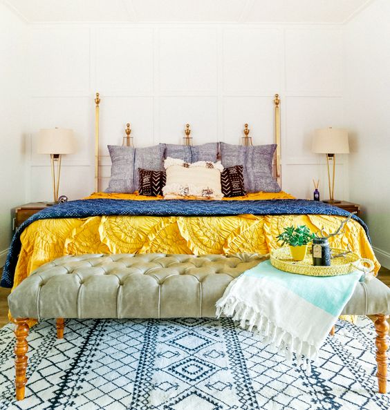 Eclectic bedroom with blue and yellow bedding, tufted bench, throw, and patterned rug